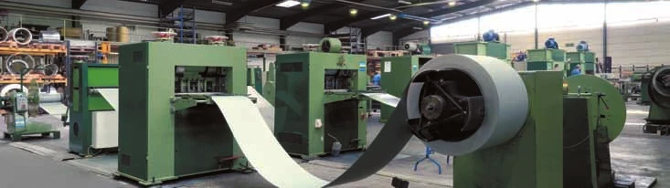 Fertigungsstraße mit Blechcoil, das in eine grüne Streckgittermaschine einläuft